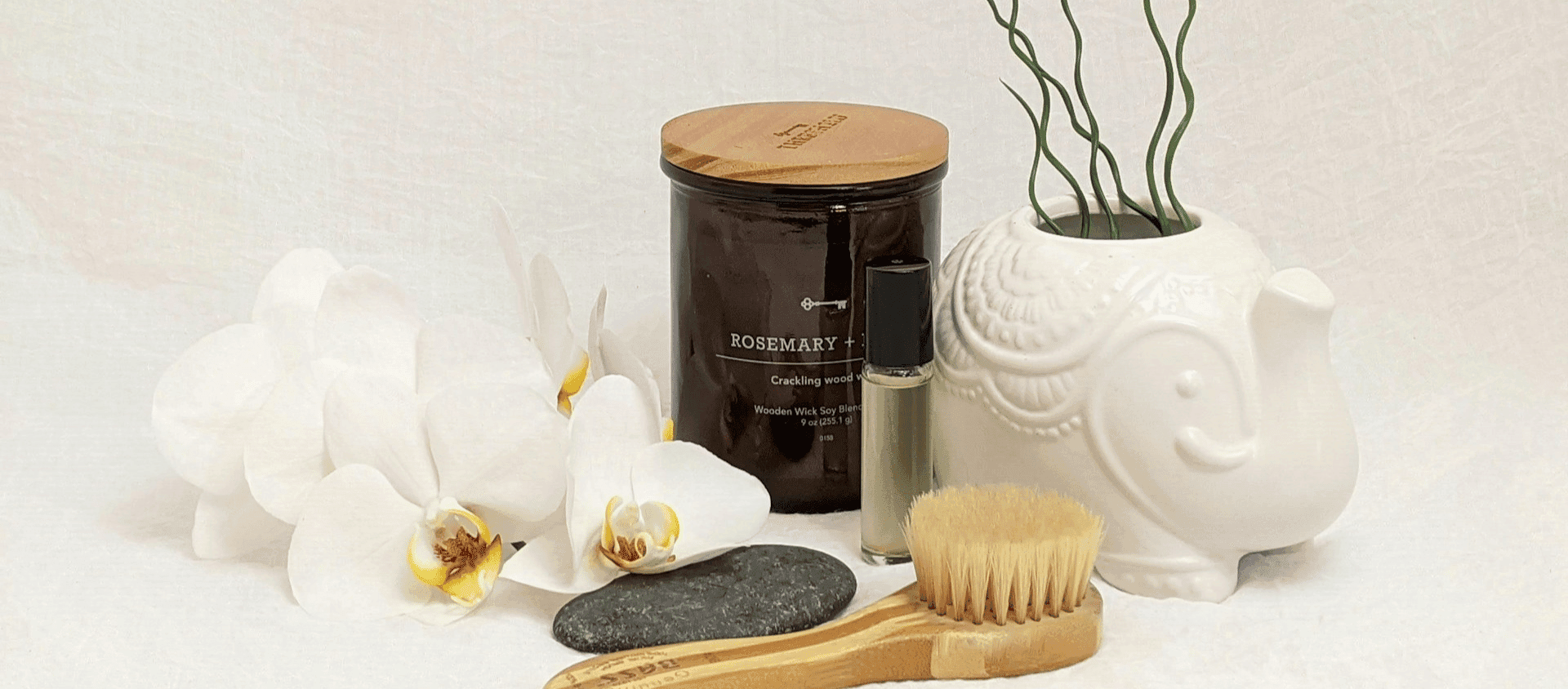 Candle, body brush, roller, and orchids arranged as a self-care pamper set.