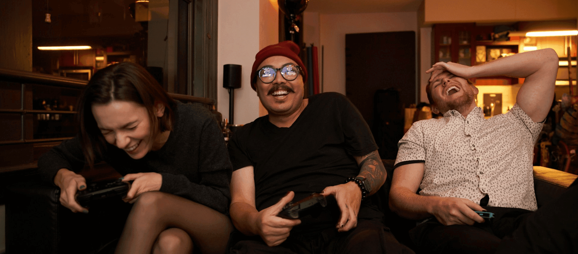 Three friends laughing while playing video games together on a couch.