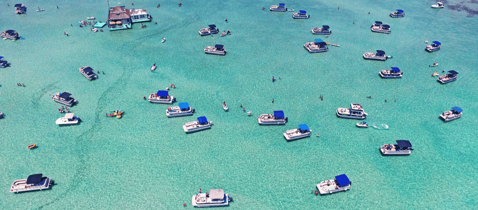 Aerial view of pontoon boats anchored in the crystal clear waters at Crab Island in Destin, Florida.