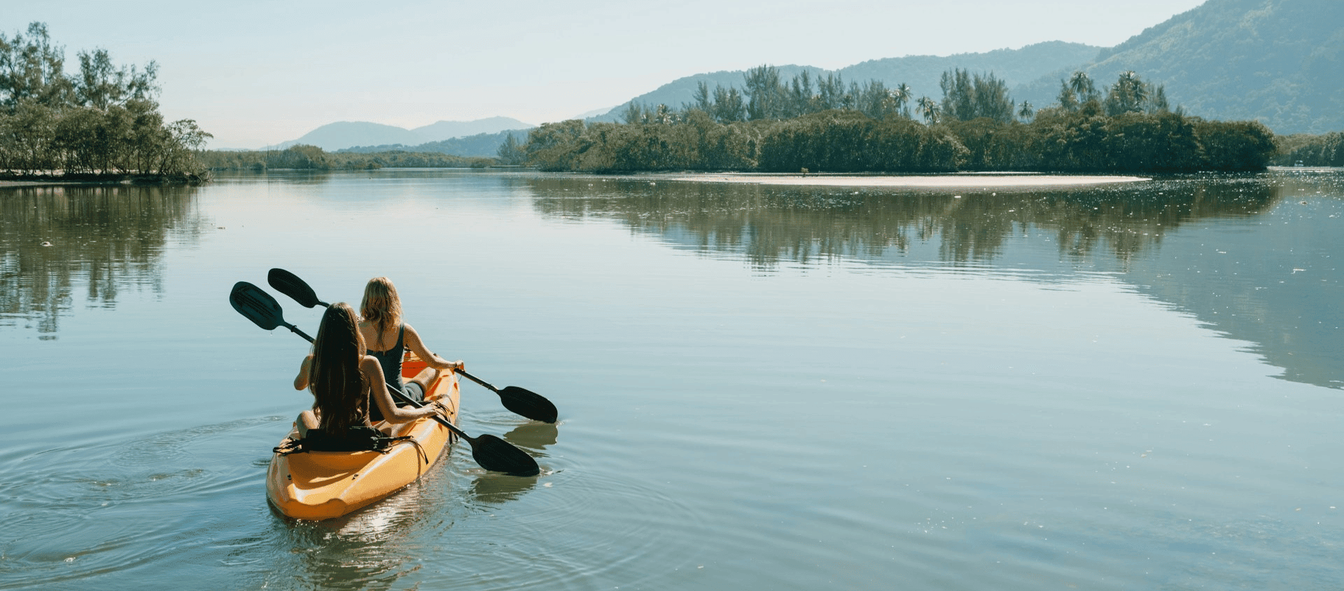 Two people kayaking on a calm lake surrounded by mountains.