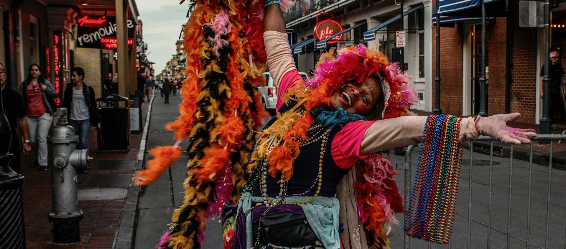 Colorful street performer dressed in feathers and beads on Bourbon Street in New Orleans.