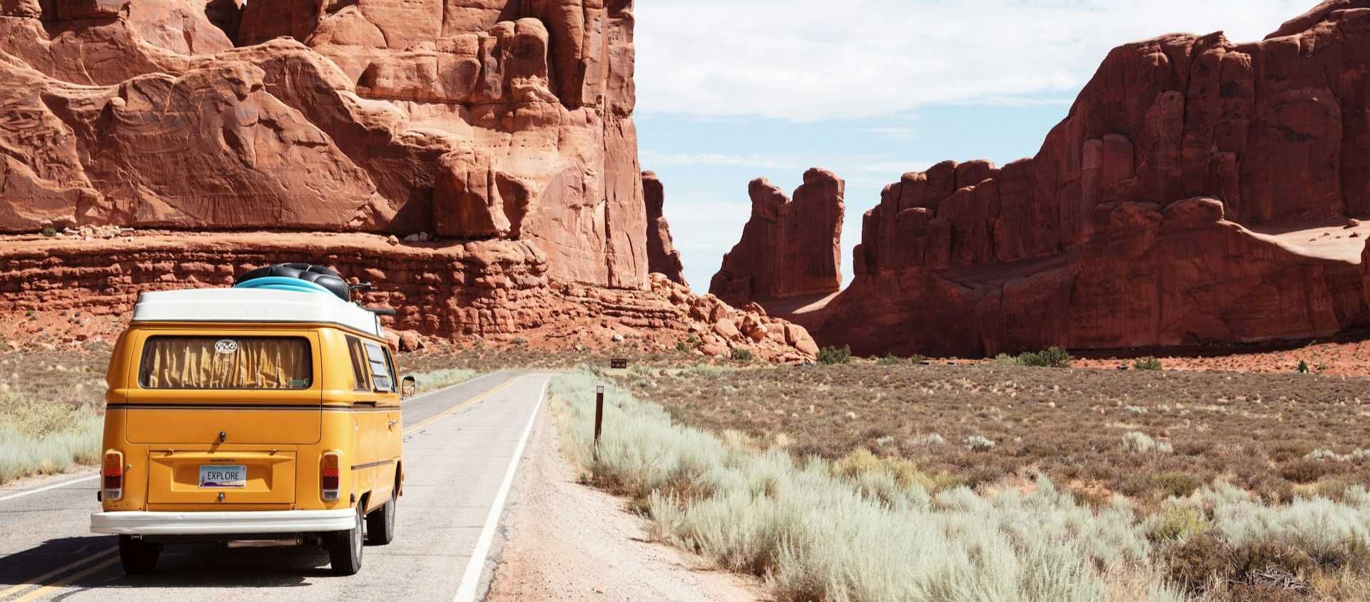 Yellow vintage camper van driving a desert road through red rock formations on a national park road trip.