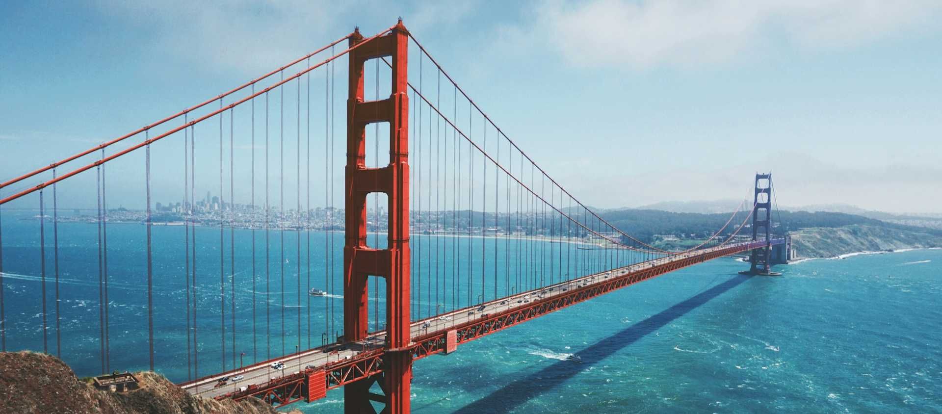 The Golden Gate Bridge spanning the bay with the San Francisco skyline in the distance on the California coast.