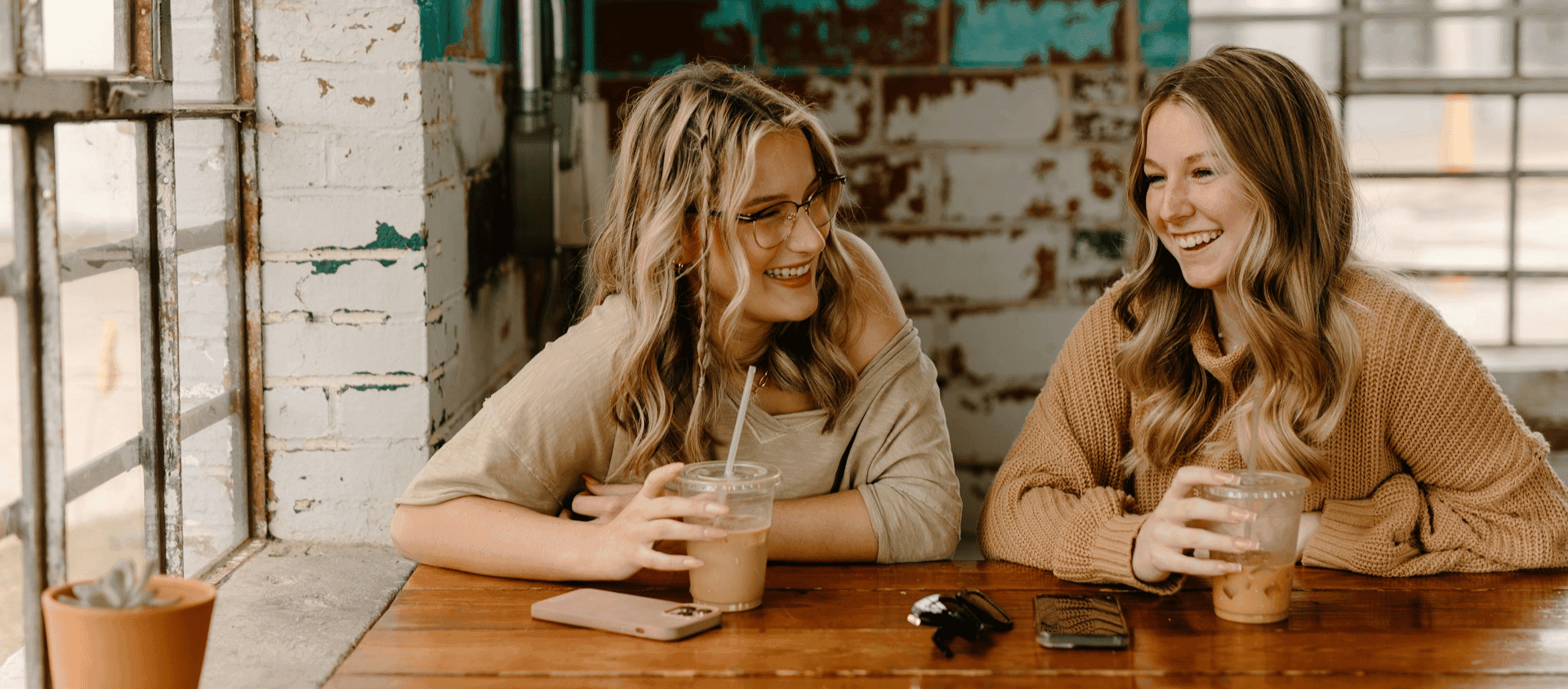 Two women laughing together while sitting at a table with iced drinks.