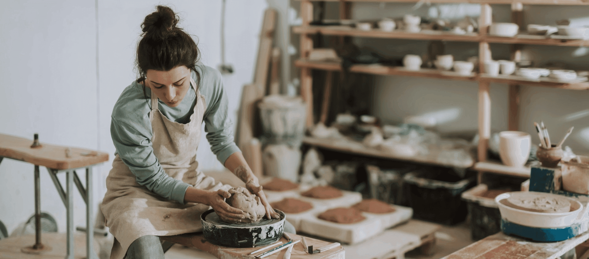 A person shaping clay on a pottery wheel in a studio.