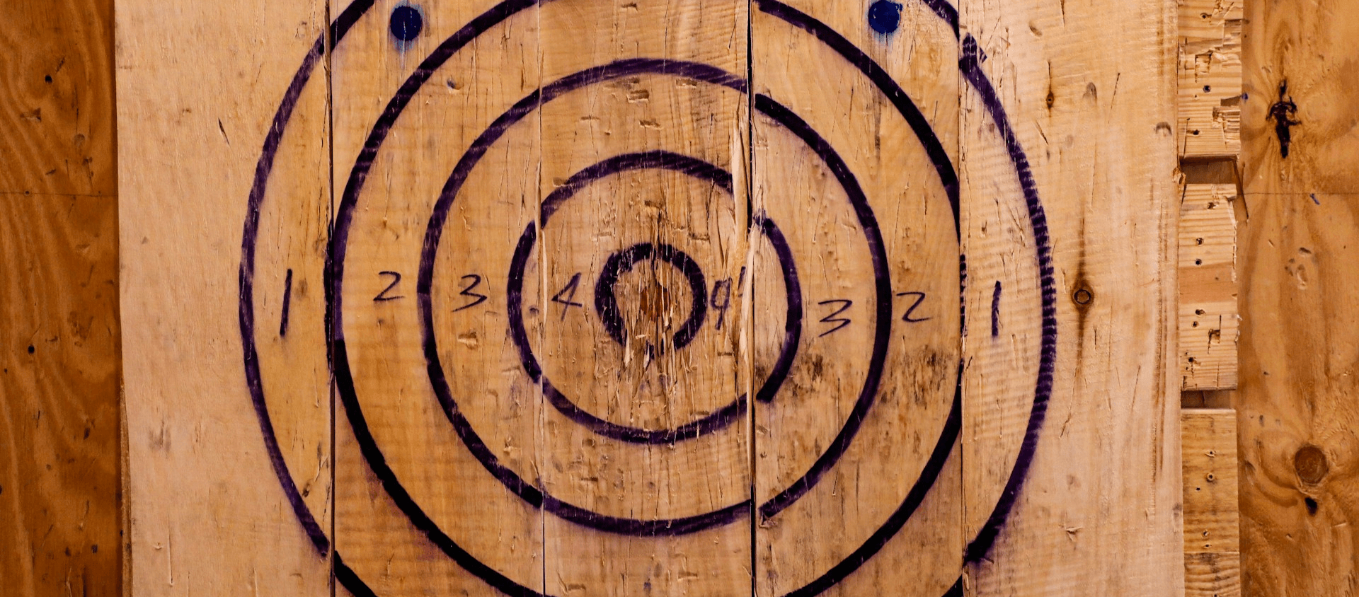 Wooden axe-throwing target with painted bullseye rings and scoring numbers on a plank wall.