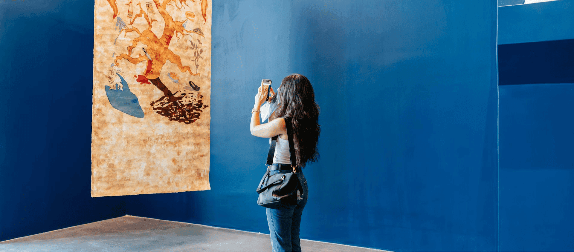 A woman photographing artwork in a gallery with blue walls.