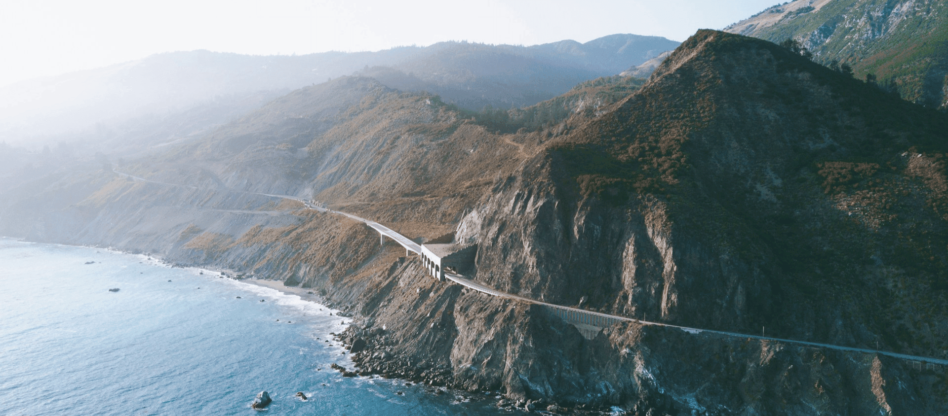 Aerial view of the Big Sur coastline with Bixby Bridge spanning a dramatic rocky canyon.