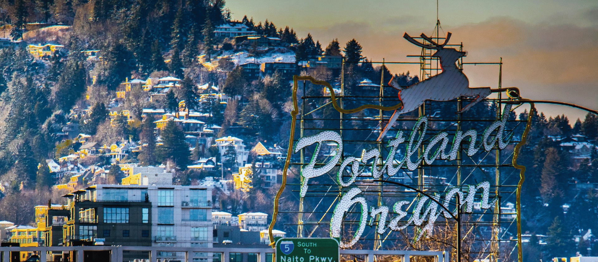 Portland Oregon neon sign with snowy hillside homes in the background.