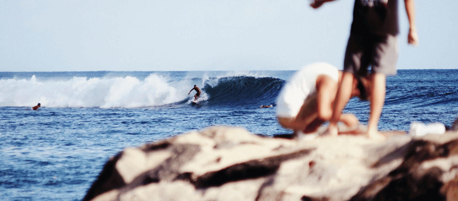 A man standing on a rock watching a surfer.
