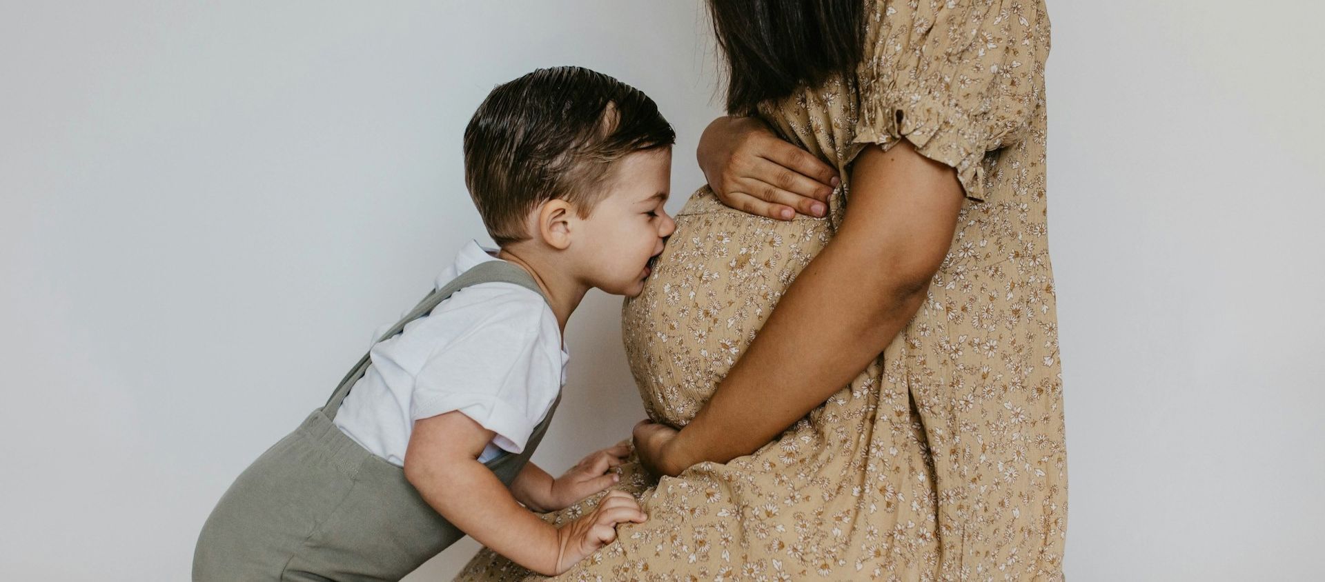 A young boy kisses his pregnant mother's belly.