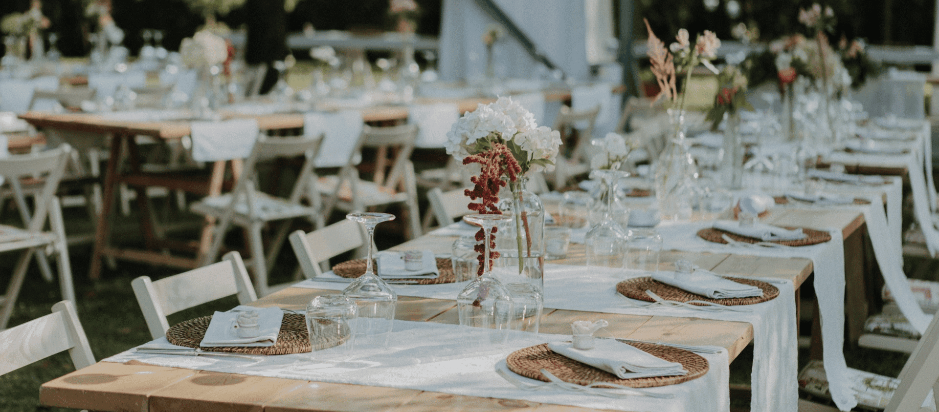 Outdoor reception tables set with white linens, glassware, and floral centerpieces.