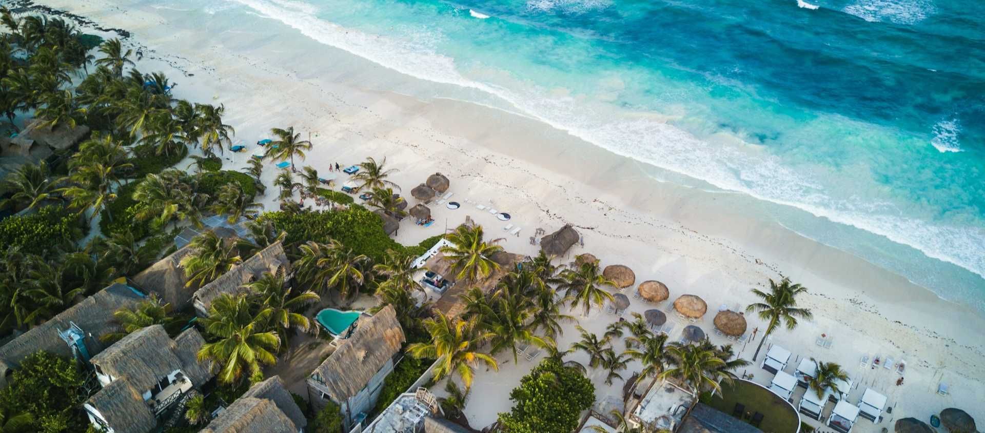 Aerial view of beachfront cabanas and turquoise water in Tulum, Mexico.