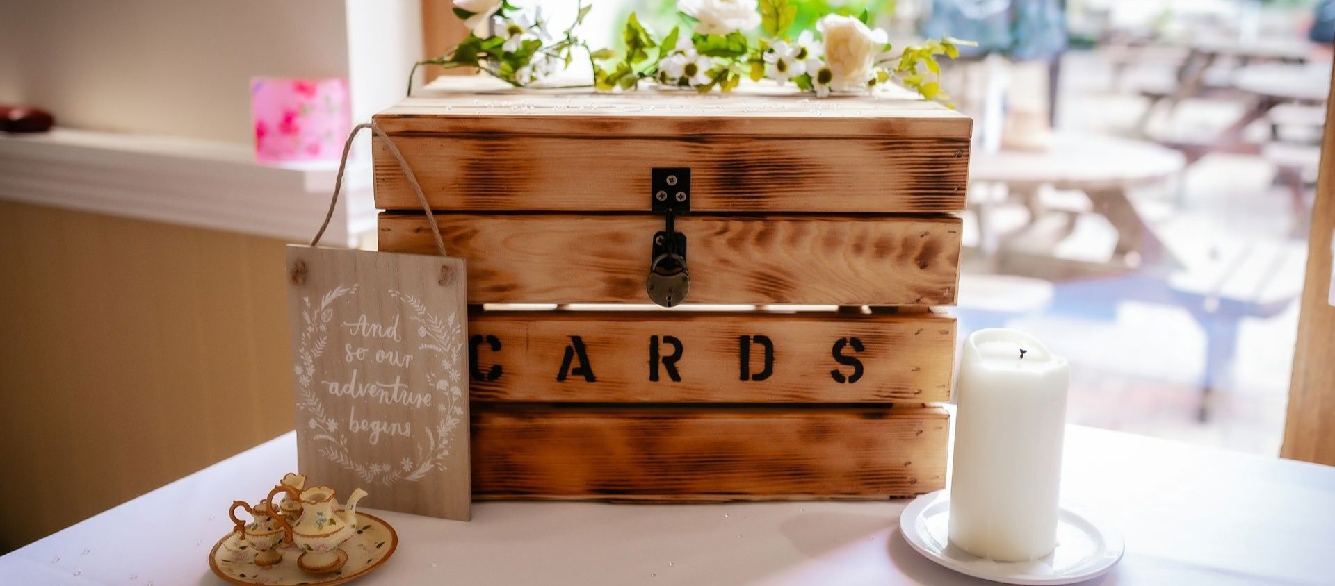 A rustic wooden wedding card box with an 'adventure begins' sign and candle.