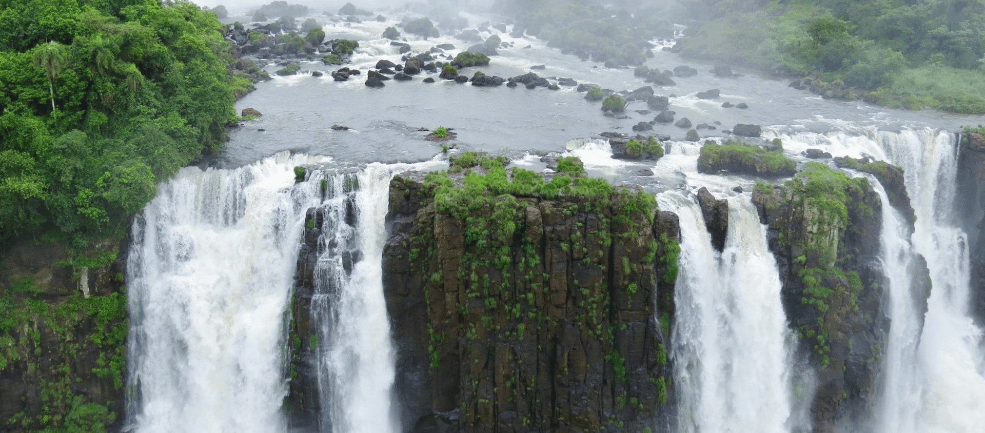 Iguaçu Falls cascading over cliffs surrounded by lush rainforest in Brazil.