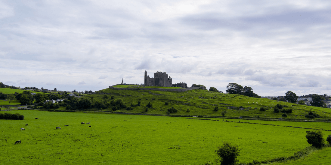 Medieval castle ruins on a grassy hilltop under a cloudy sky in Ireland.