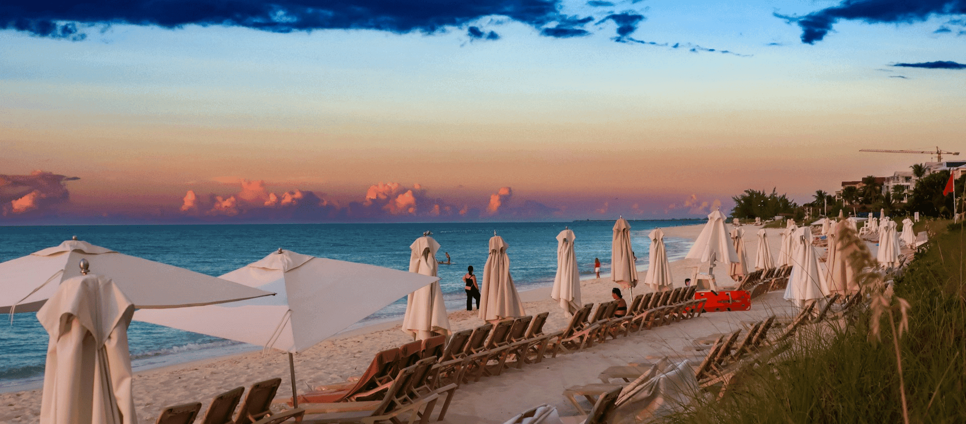 White umbrellas and lounge chairs lining a Grace Bay beach at sunset in Turks and Caicos.