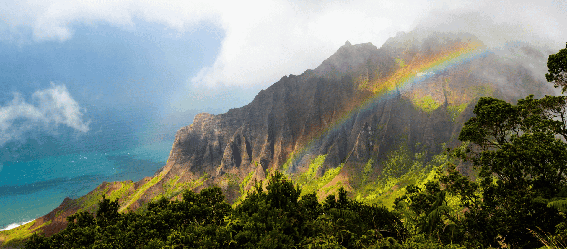 Dramatic Kauai cliffs with rainbow over lush green mountains in Hawaii.