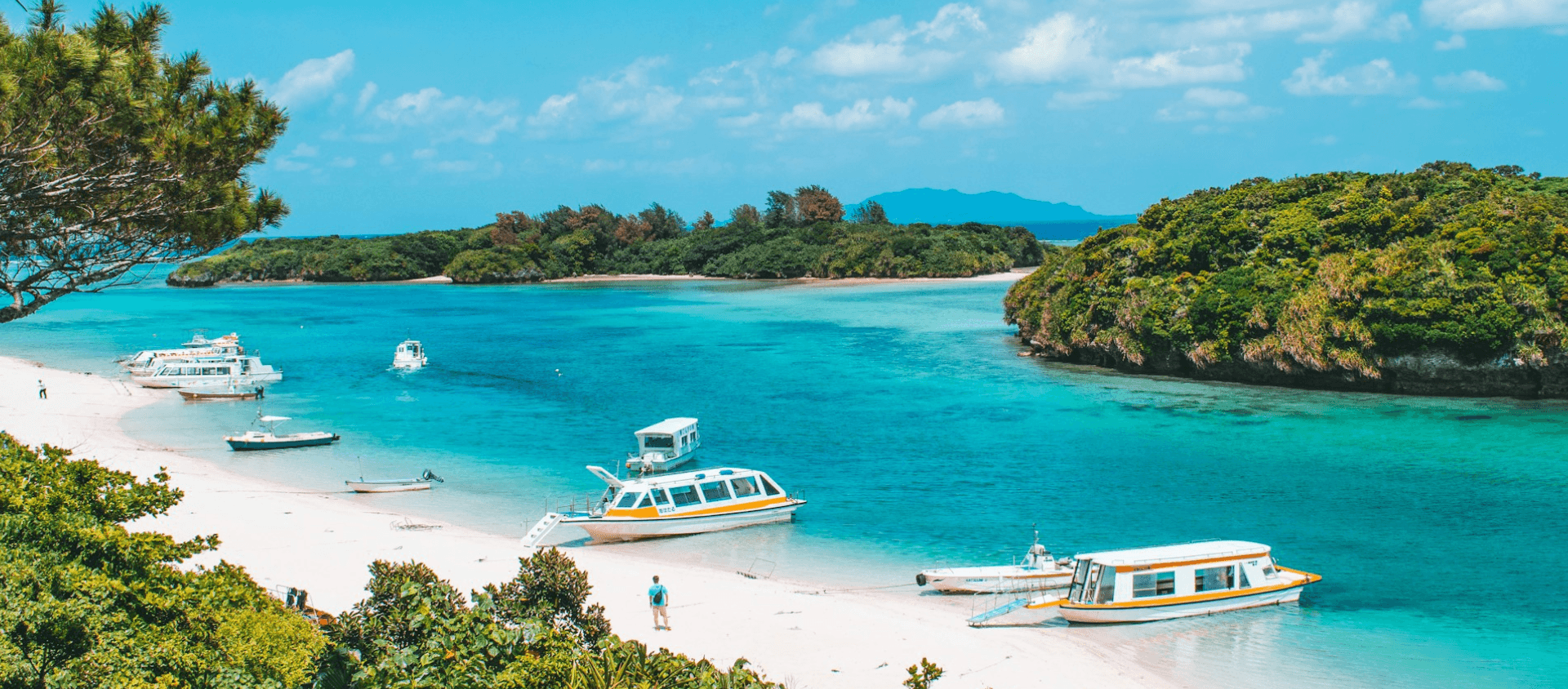 Boats on a turquoise bay with white sand beach and green islands.