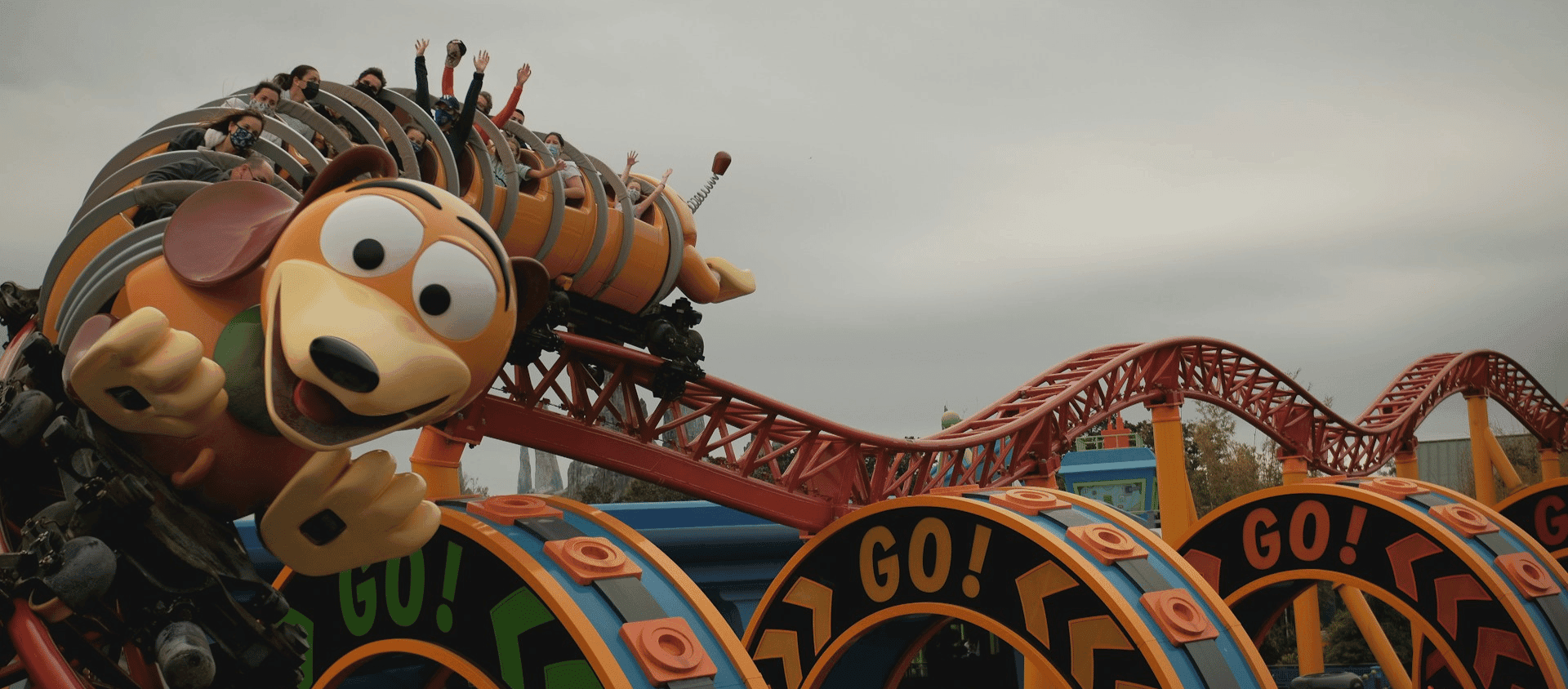 Roller coaster shaped like a cartoon dog with riders raising their hands.