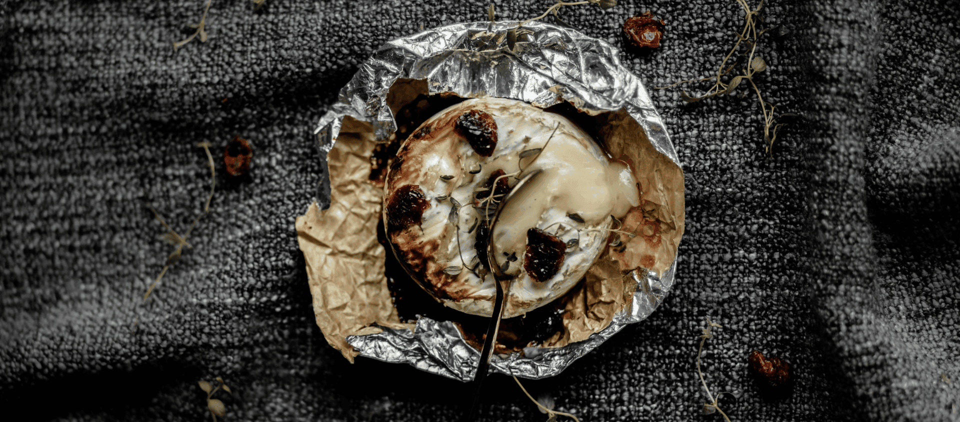 Baked brie topped with herbs and garlic served with bread on parchment.