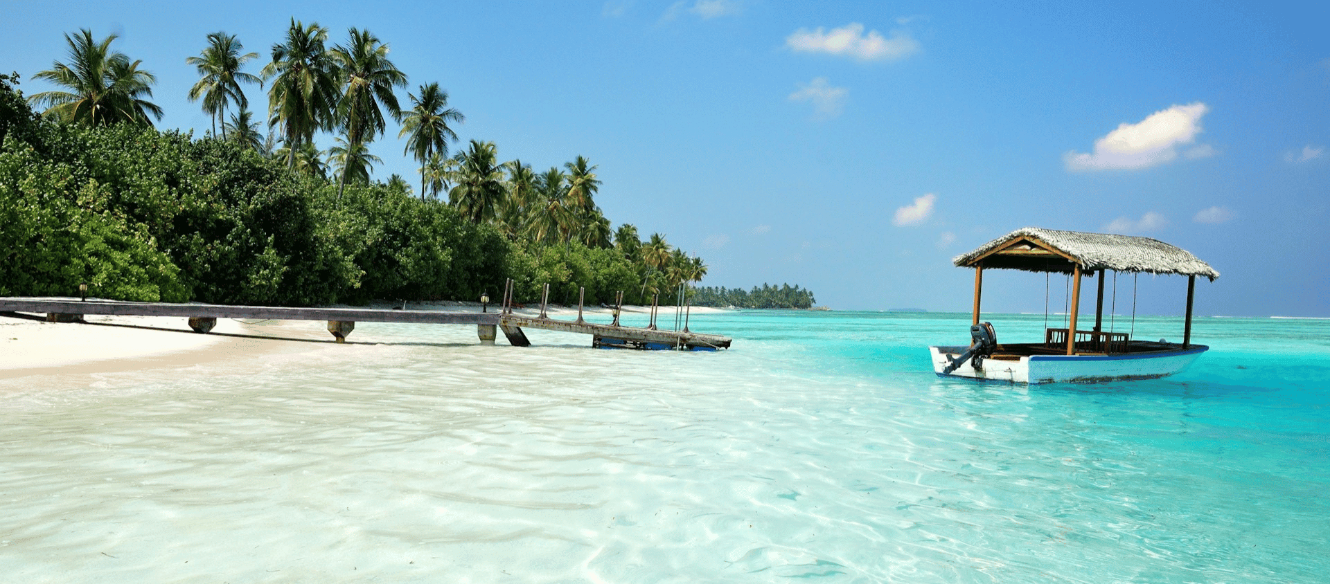 Traditional island boat anchored in crystal clear shallow water beside a palm lined tropical shoreline.