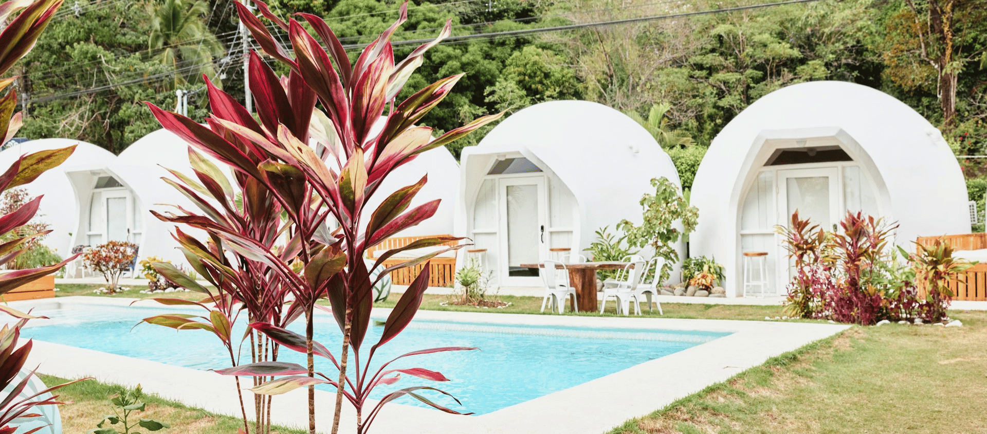 Modern white dome-shaped cabins with a swimming pool and tropical plants in front.