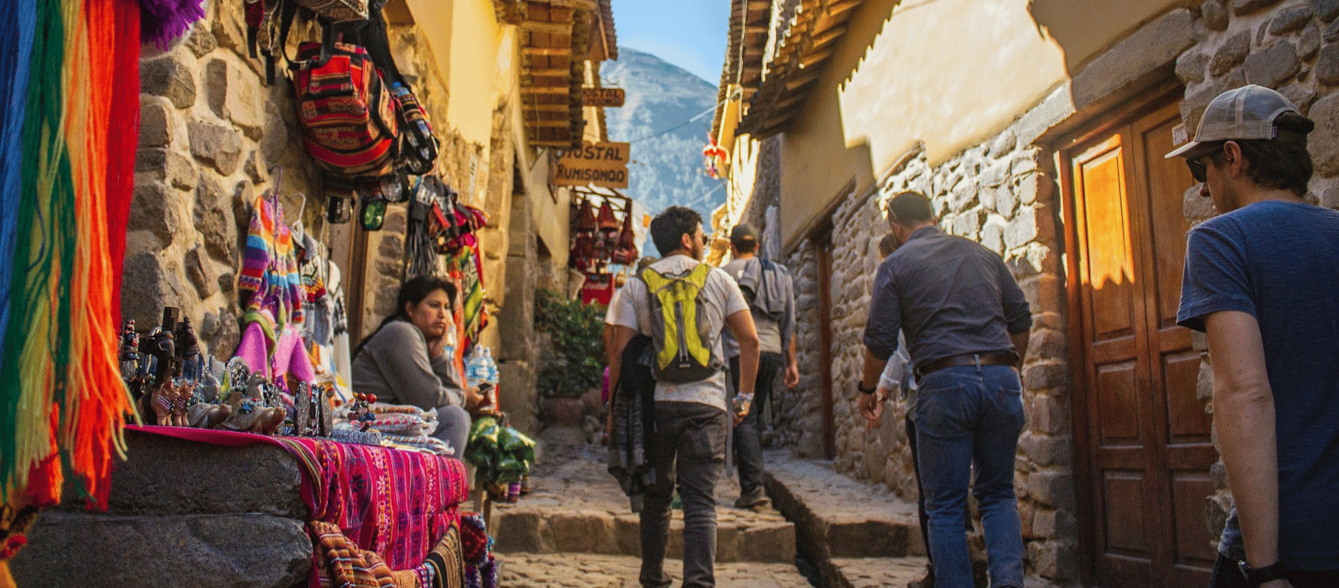 Travelers walking through a market-lined cobblestone street in the Sacred Valley near Cusco.