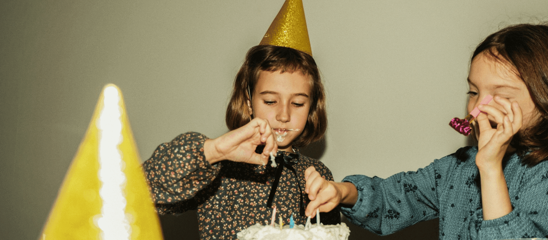 Two children wearing party hats decorating a birthday cake together.