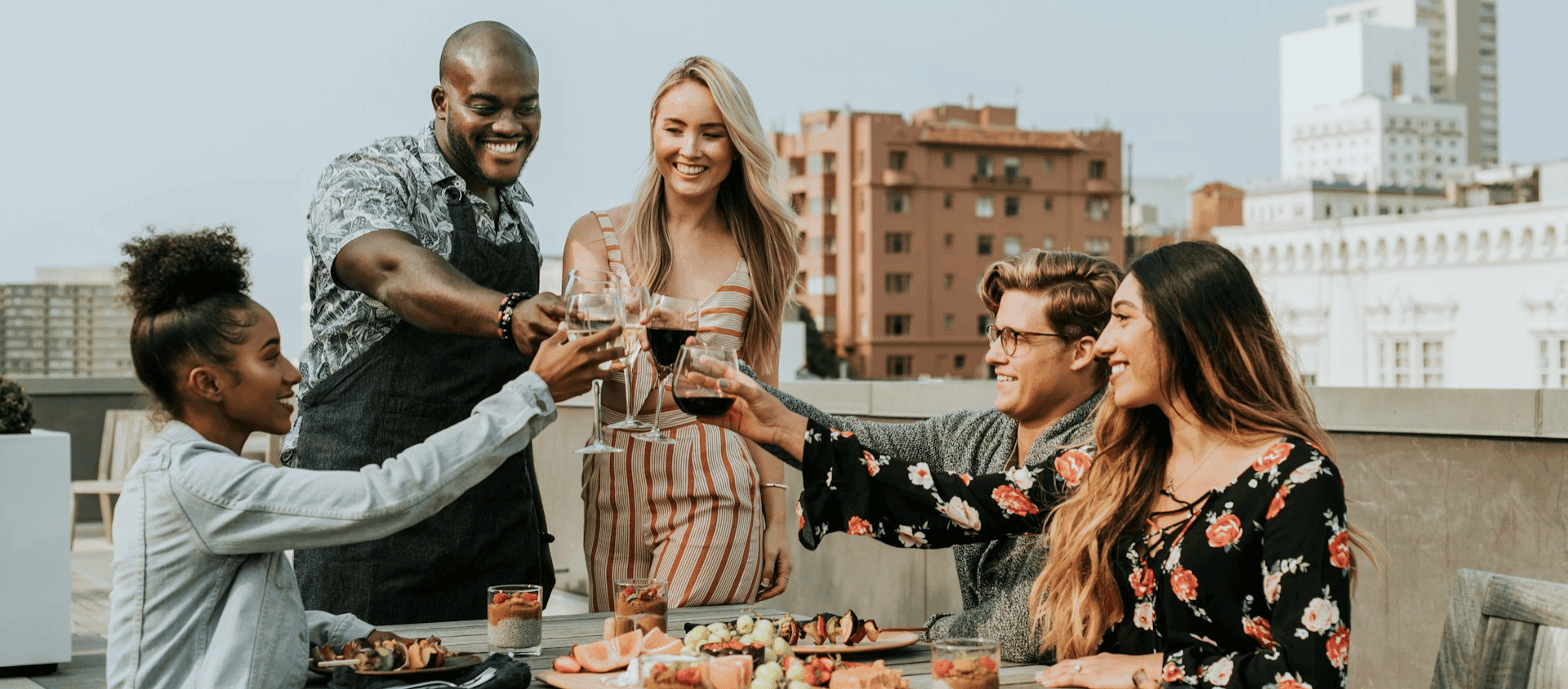 Group of friends toasting with wine glasses at an outdoor rooftop gathering.