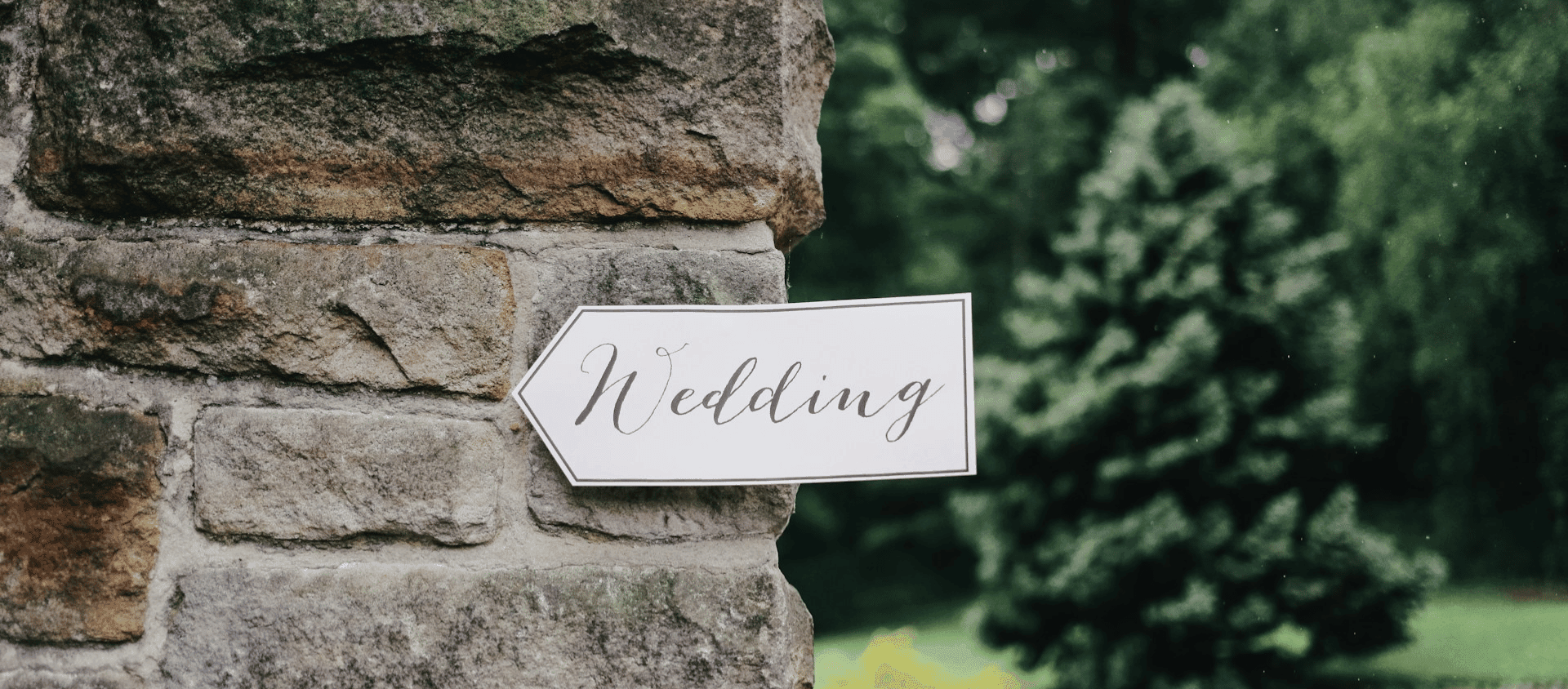 A wedding sign mounted on a stone wall pointing toward the venue.