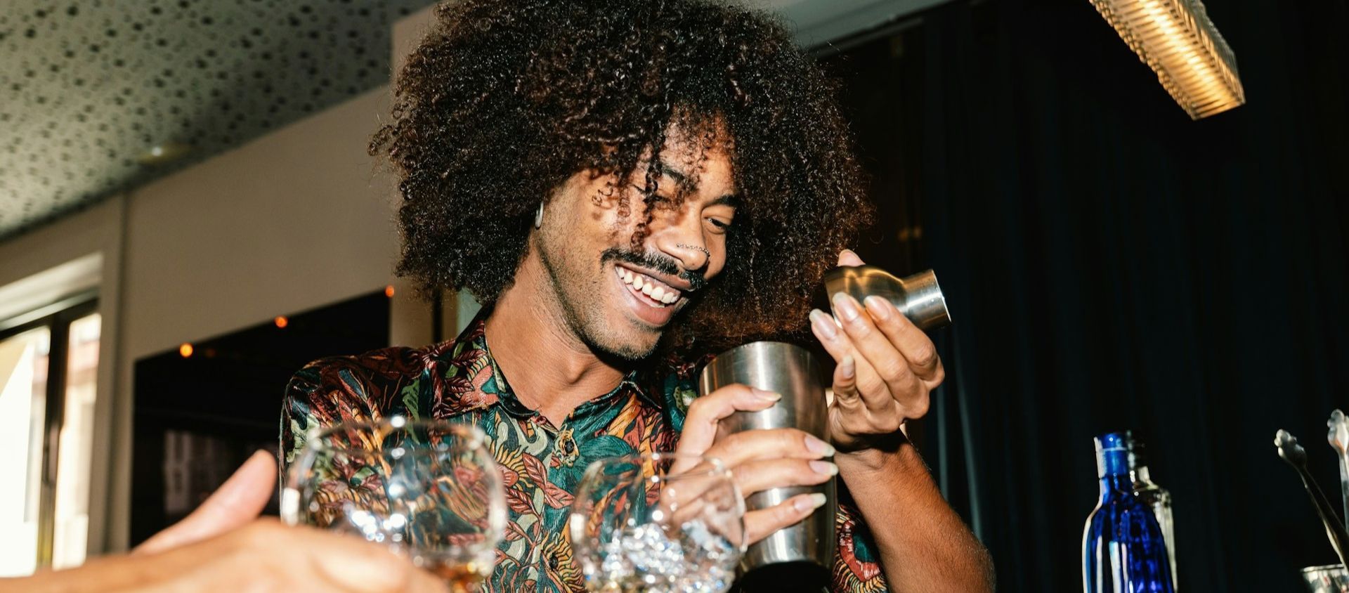 Smiling man measuring a drink with a cocktail shaker at a home bar.