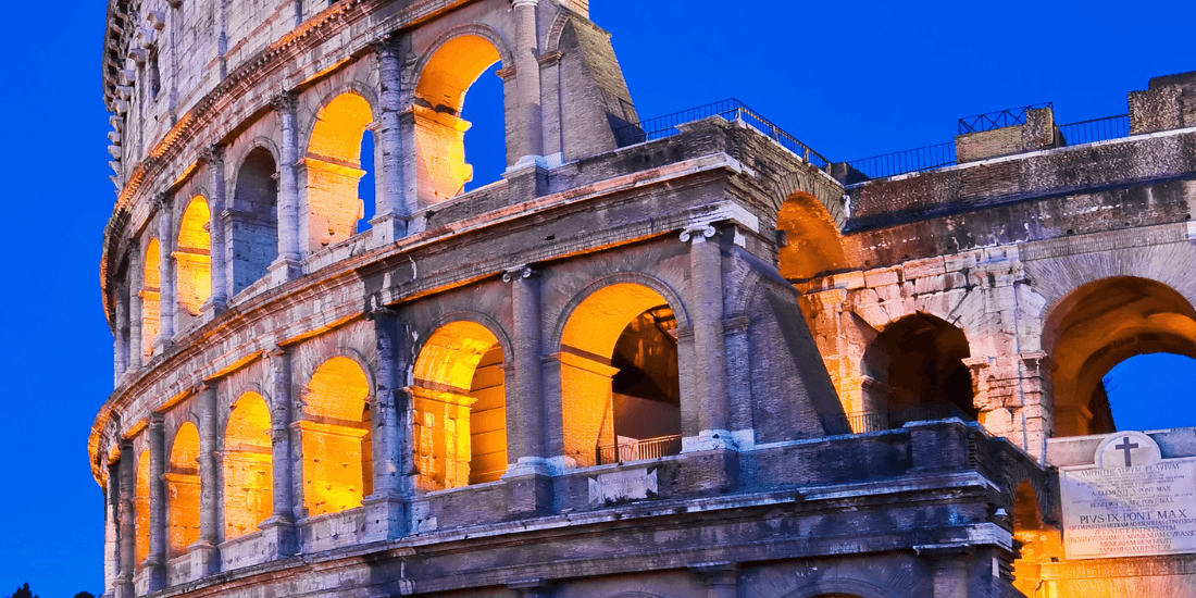The Colosseum in Rome illuminated at night against a deep blue sky.