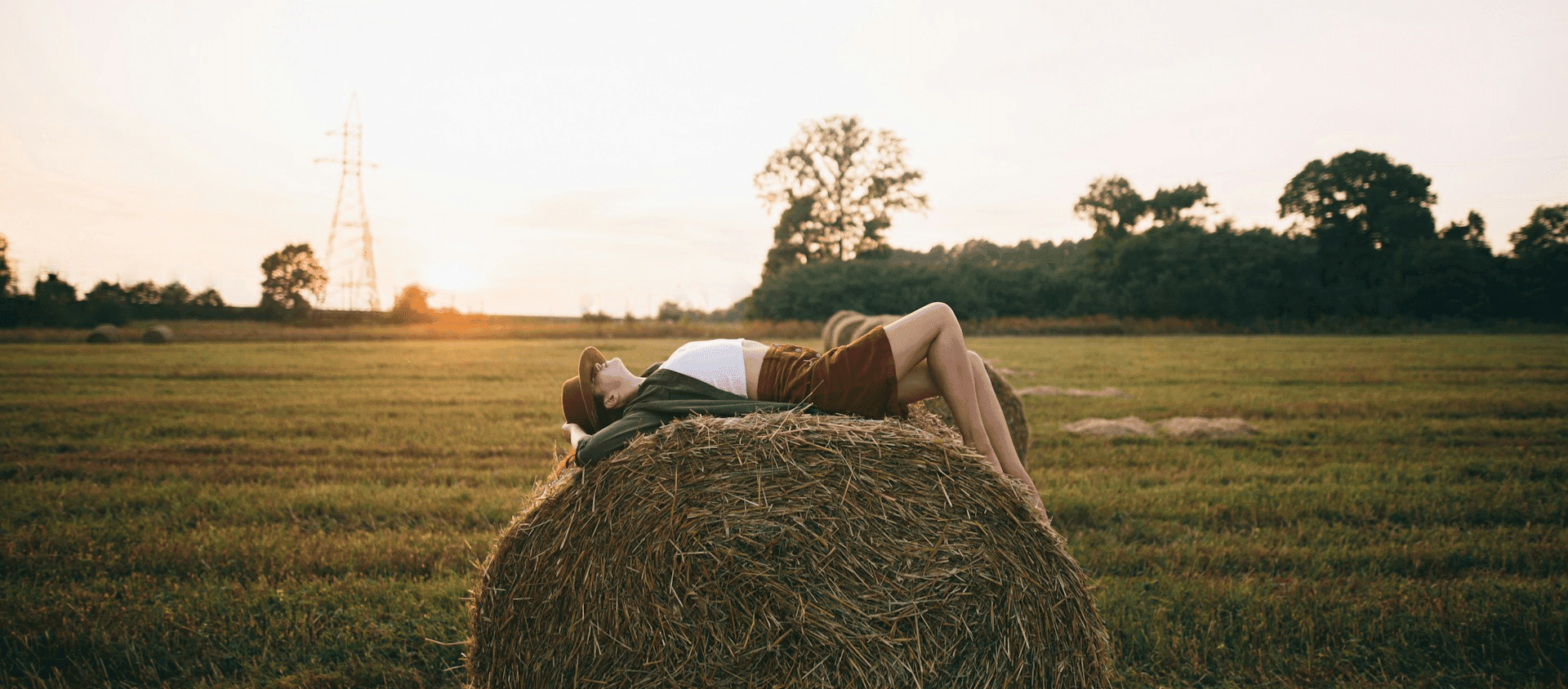 woman laying on top of barrel of hay in open field with sunset in background