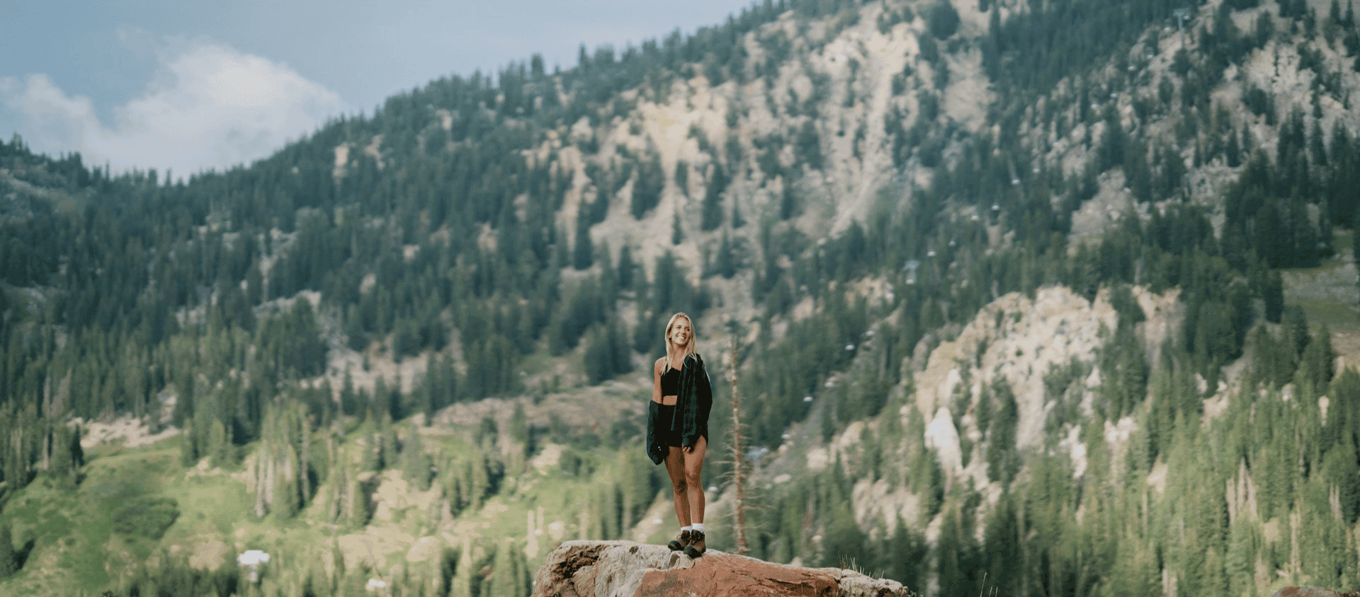 Woman standing on a mountain ridge overlooking a forested valley near Denver.