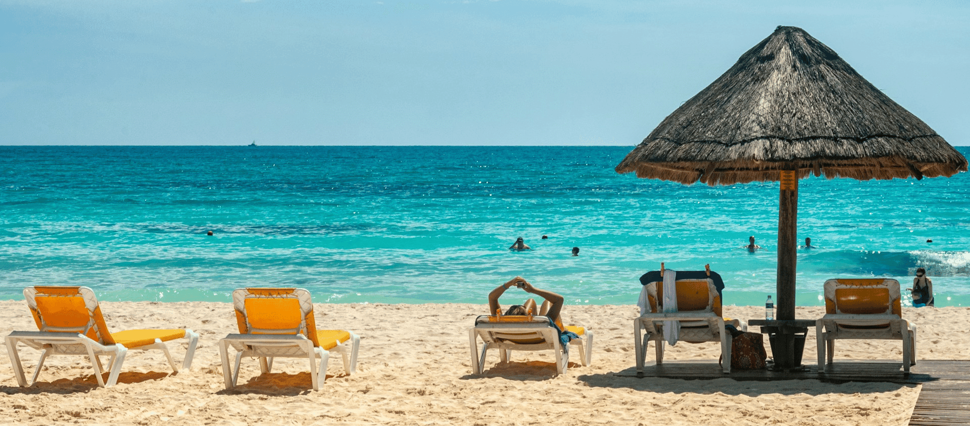 Beach lounge chairs and a palapa umbrella on the turquoise shoreline in Cancun, Mexico.