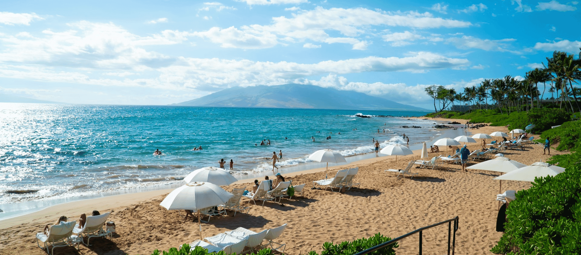 White umbrella beach chairs lined along the turquoise shoreline of Wailea, Maui.