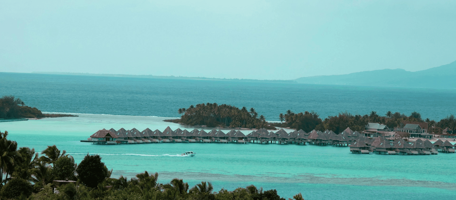 Aerial view of thatched-roof overwater bungalows at a luxury Tahiti resort.