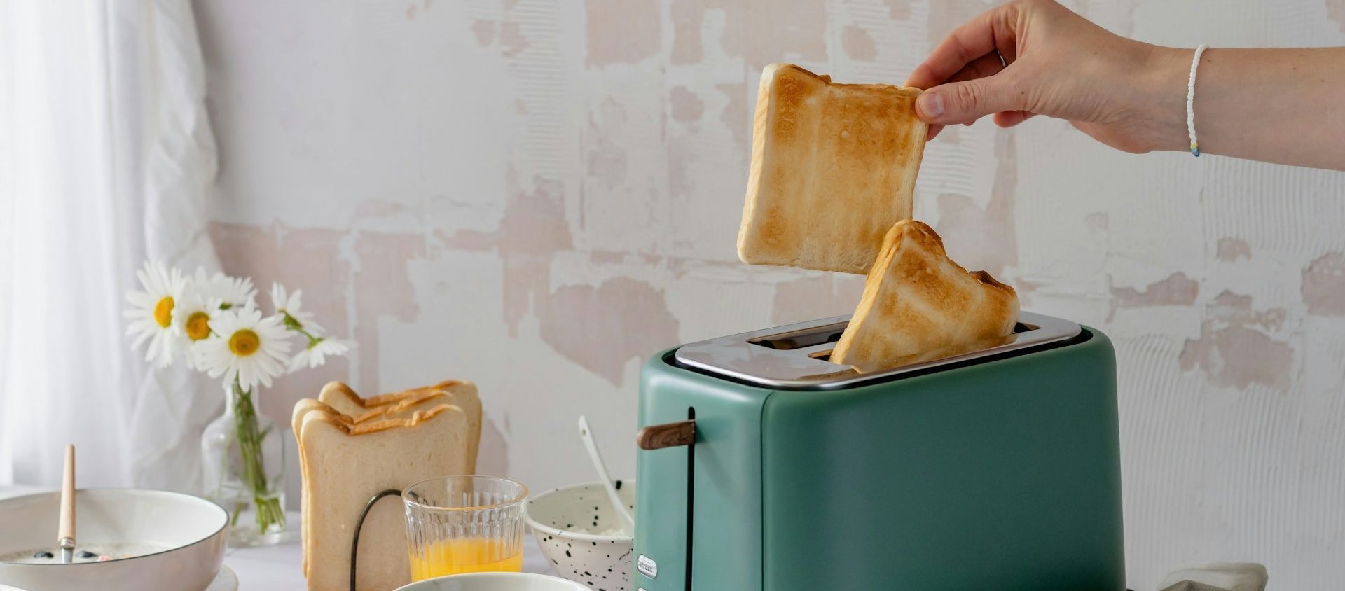 A hand lifts toast from a green toaster on a breakfast table.