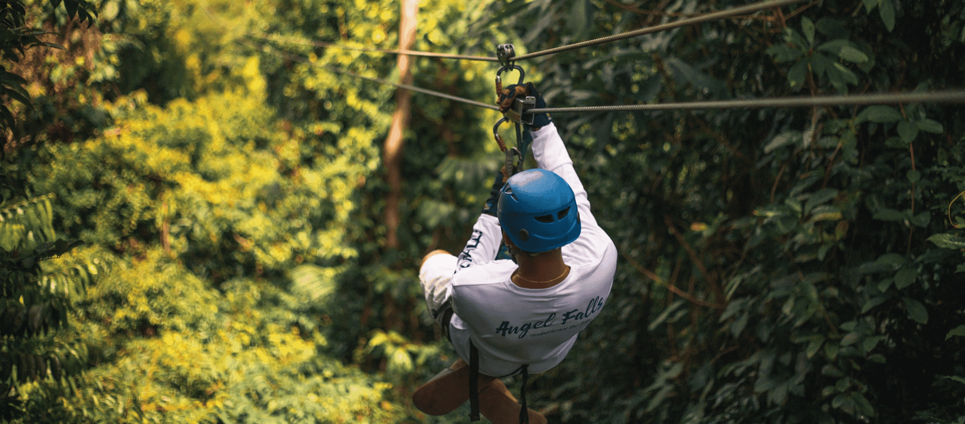 A person ziplining through the dense green rainforest canopy in inland Belize.