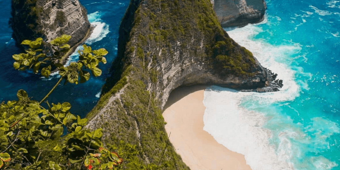 Steep coastal cliffs enclosing a crescent-shaped sandy beach with turquoise waves.
