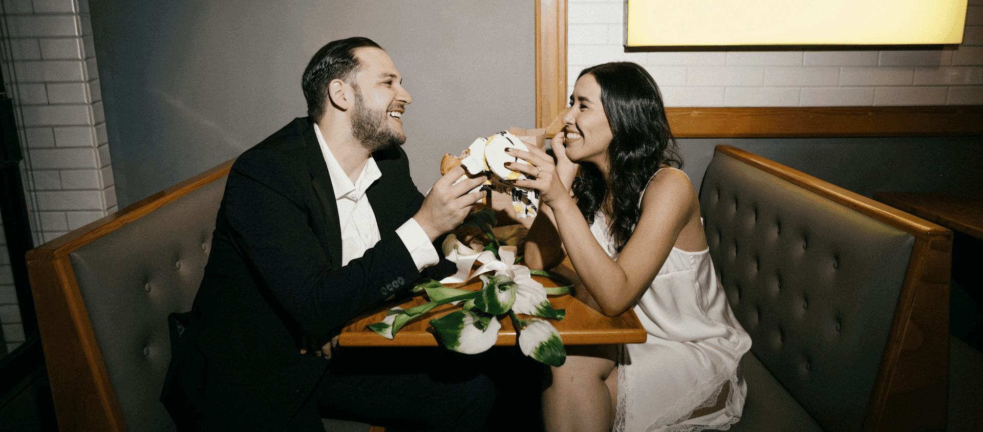 Couple laughing and sharing food while seated in a restaurant booth.
