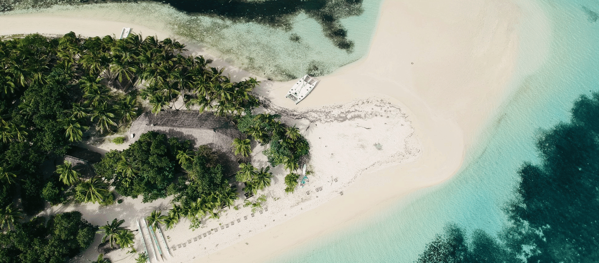 Aerial view of a tropical island with palm trees, white sand beach, and shallow turquoise water.