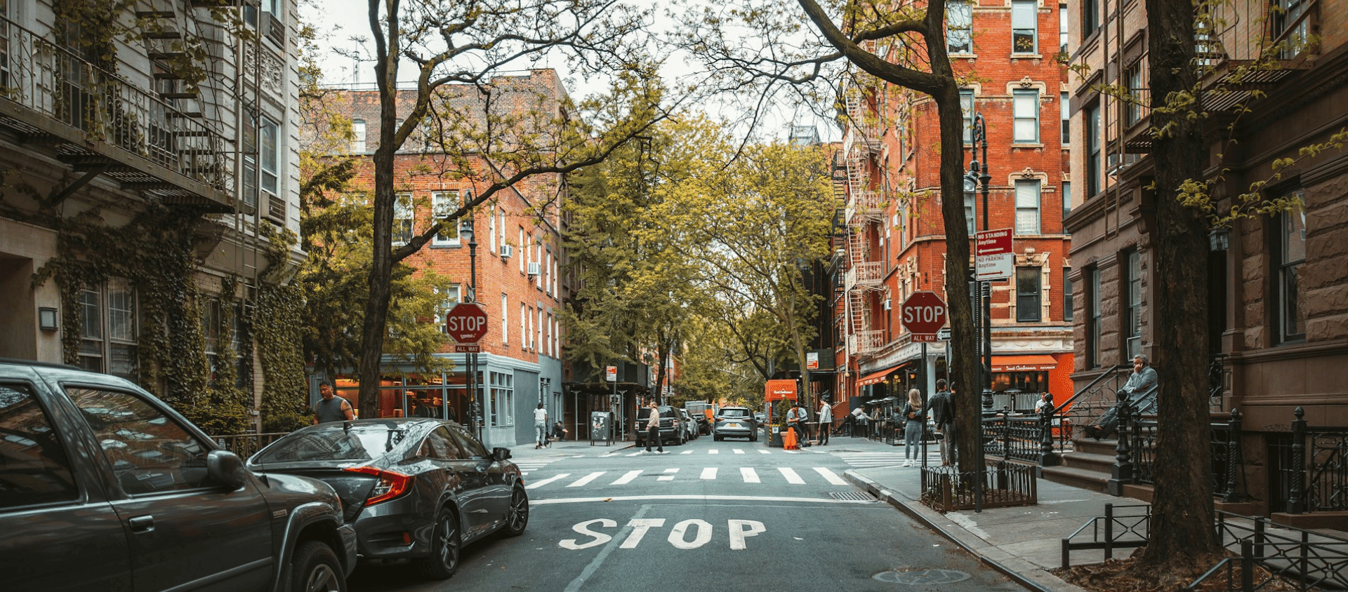 Tree lined residential street in Manhattan with brownstones and stop signs.