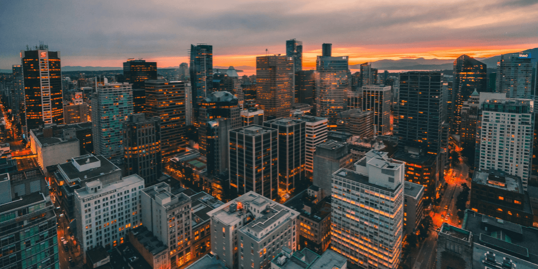 City skyline at dusk with office buildings lit against a sunset sky.