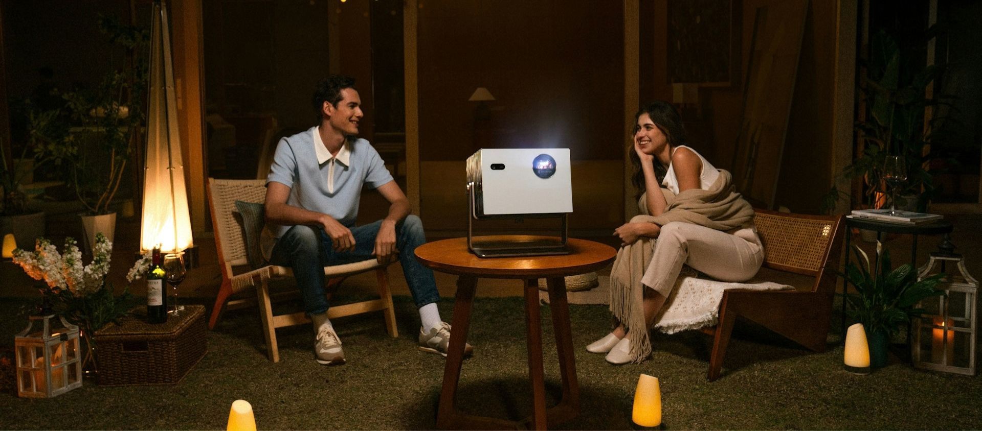 A couple relaxing outdoors watching a movie on a projector screen.