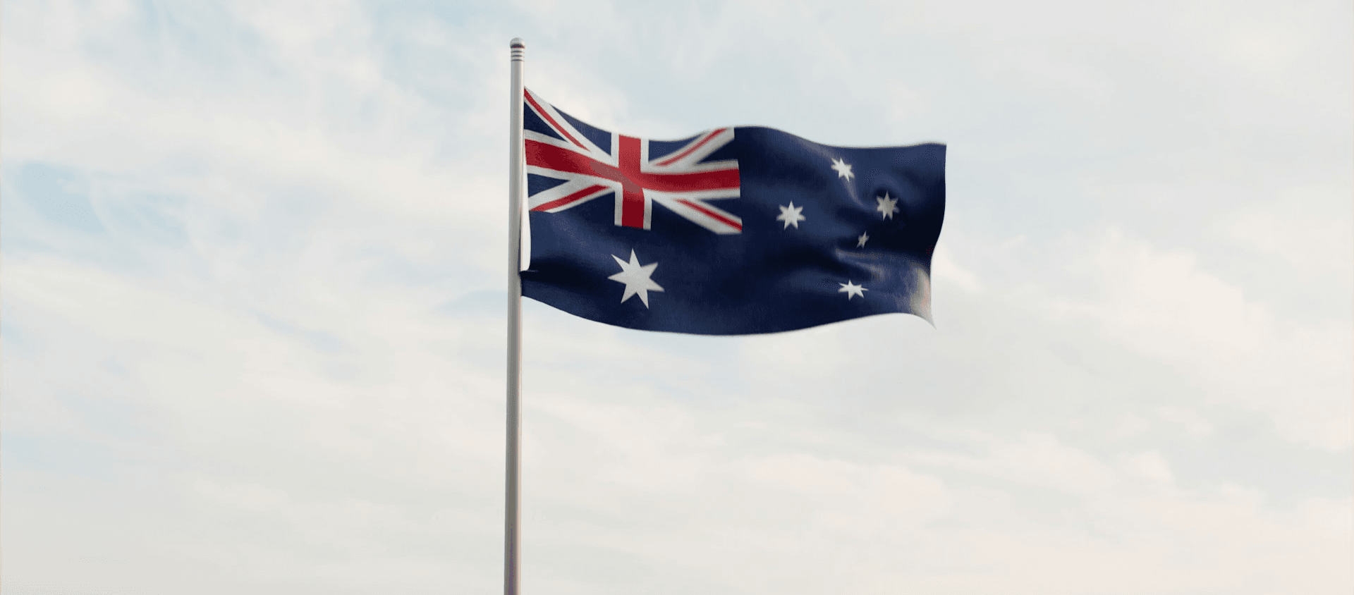 Australian flag waving on a flagpole against a cloudy sky.