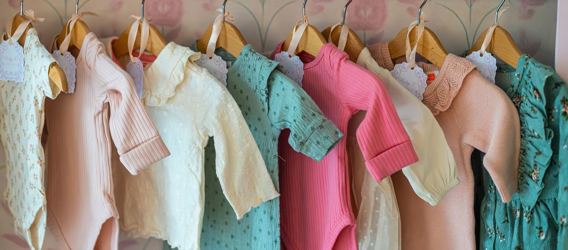 A row of pastel baby onesies hanging on wooden hangers.