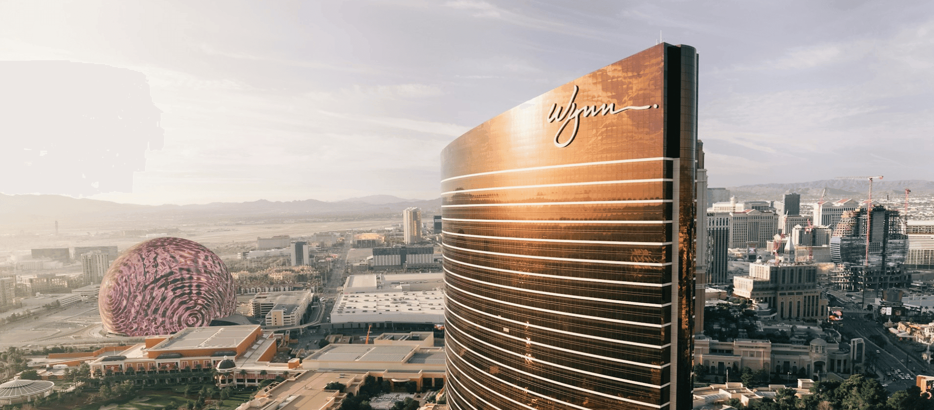 Wynn Las Vegas hotel tower at dusk with the MSG Sphere glowing in the background.