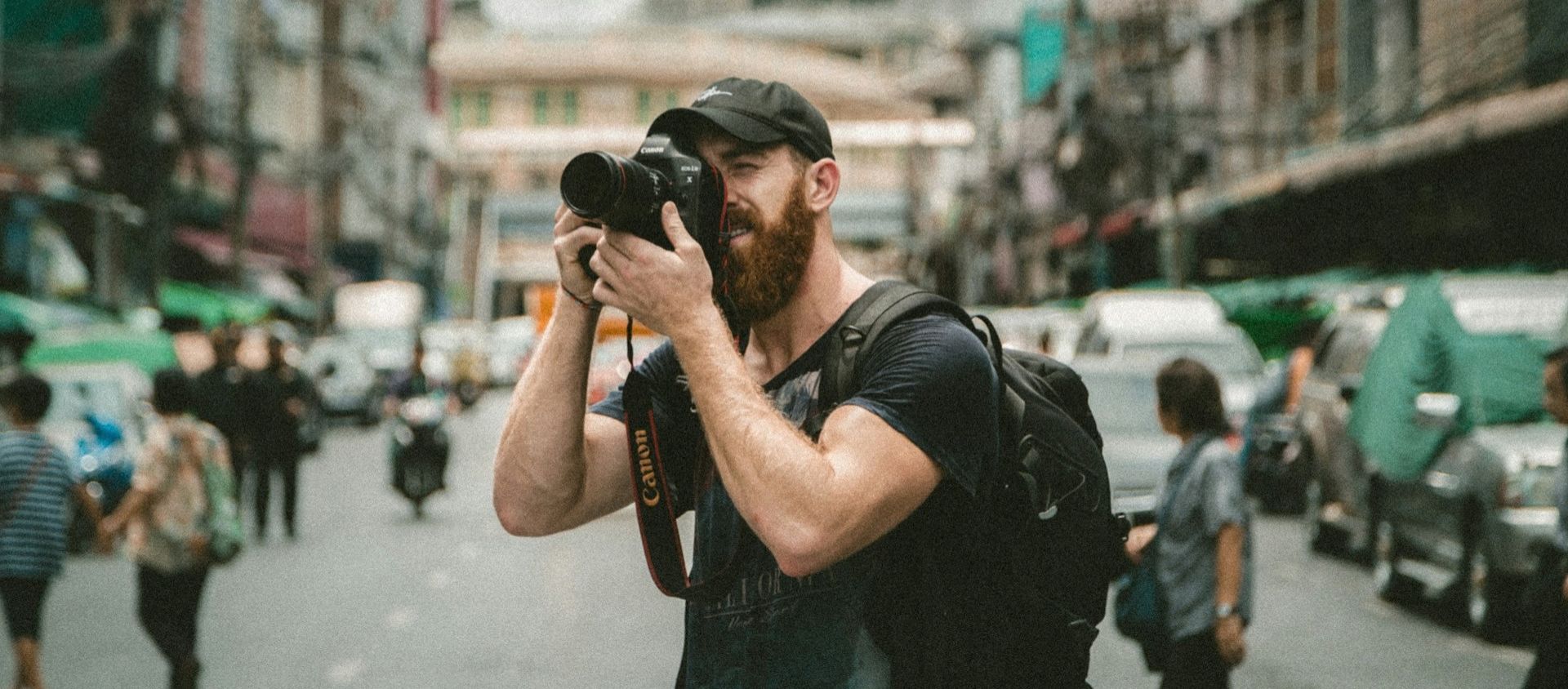 Man using a DSLR camera on a busy city street.